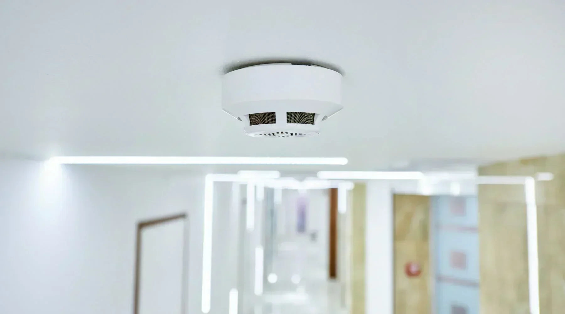 a modern carbon monoxide detector mounted in a home hallway with a family/home environment in soft focus.