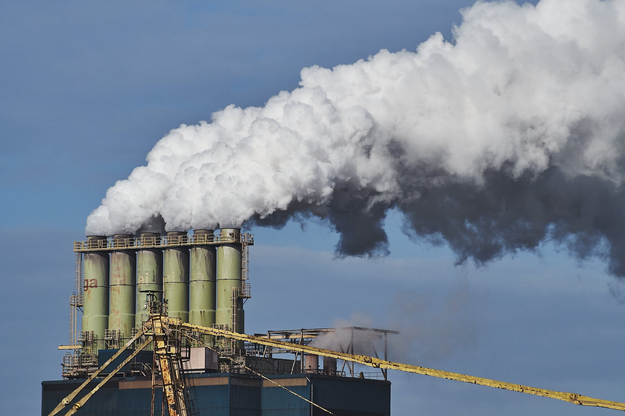 Industrial factory chimneys emitting thick white smoke into the sky, highlighting air pollution and environmental impact.