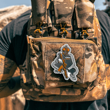Close up Back view of Male wearing a tactical plate carrier with Slav Squat morale patch velcroed to front chest while holding an AR-style rifle. Also wearing TAPR with P-CAN