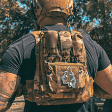 Back view of Male wearing a tactical plate carrier with Slav Squat morale patch velcroed to front chest while holding an AR-style rifle. Also wearing TAPR with P-CAN