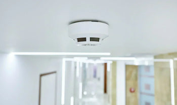 a modern carbon monoxide detector mounted in a home hallway with a family/home environment in soft focus.