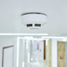 a modern carbon monoxide detector mounted in a home hallway with a family/home environment in soft focus.