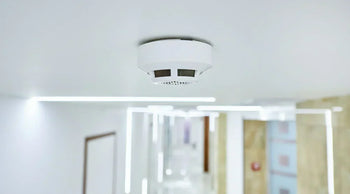 a modern carbon monoxide detector mounted in a home hallway with a family/home environment in soft focus.