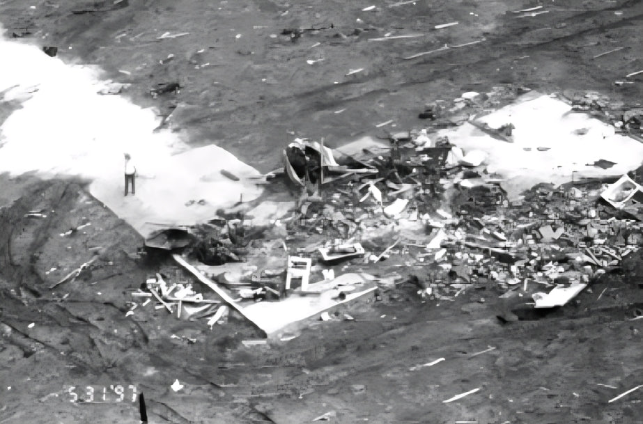 Aerial view of tornado destruction showing debris, collapsed structures, and emergency response foam on the ground after a powerful storm in a rural area.