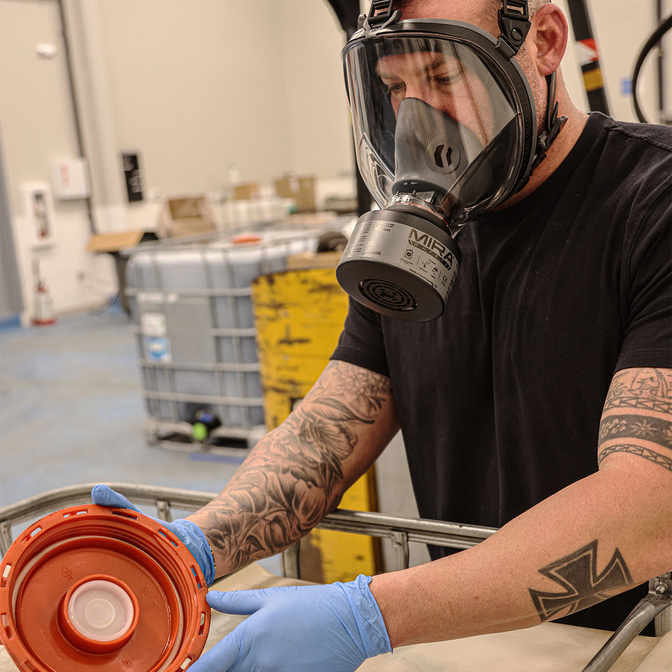 Man cleaning out a container lid with gloves on, wearing a CM-I01 respirator with a NBC-77 SOF filter attached.