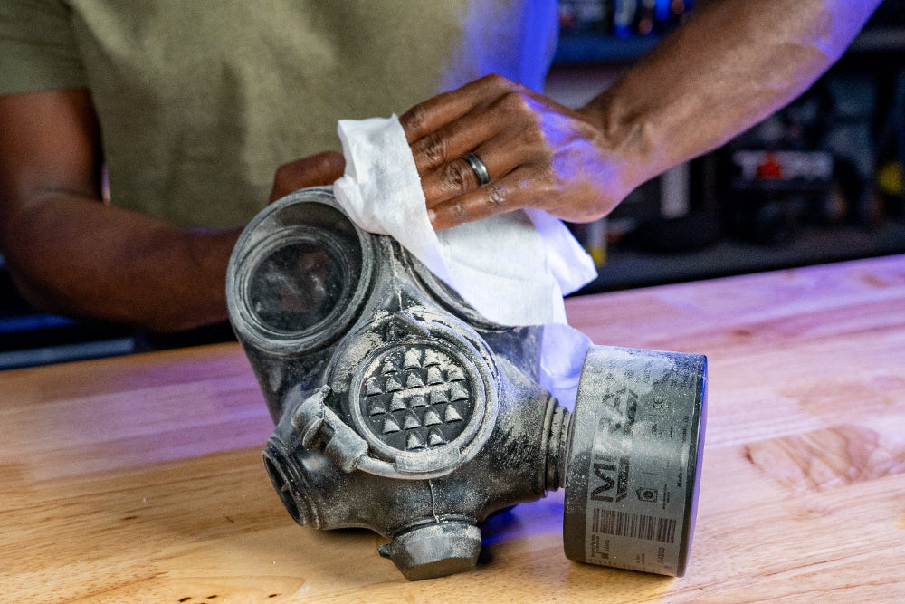 Person cleaning a vintage gas mask with a cloth on a wooden surface