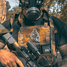 Male wearing a tactical plate carrier with Slav Squat morale patch velcroed to front chest while holding an AR-style rifle. Also wearing TAPR with P-CAN