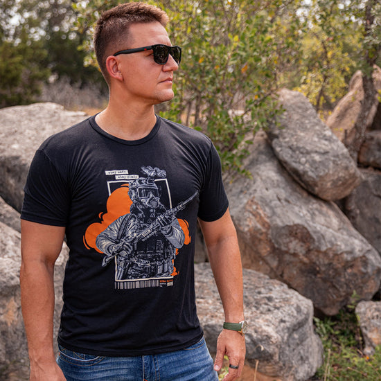 A side profile medium shot of a man wearing the  "Stay Safe, Stay Ready" T shirt standing outdoors, in front of rocks.