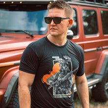 A side profile medium shot of a man wearing the "Stay Safe, Stay Ready" T shirt standing outdoors, in front of a red jeep.