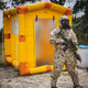 A soldier wearing a MOPP suit is guarding the decontamination shower with an AR-15 rifle.