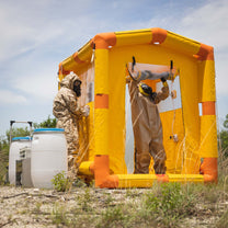 A man in a hazmat suit is exiting through the back end of the decontamination shower.